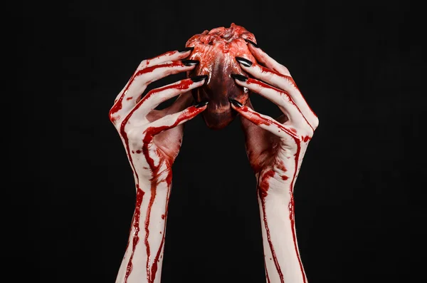 Horror sangrento e tema de Halloween: mãos sangrentas terríveis com unhas pretas segurando um coração humano sangrento em um fundo preto isolado em estúdio — Fotografia de Stock