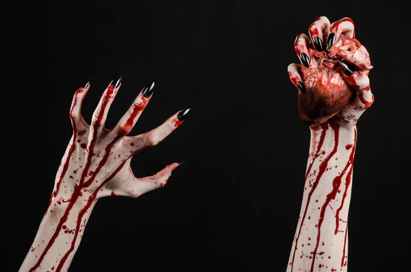 Horror sangrento e tema de Halloween: mãos sangrentas terríveis com unhas pretas segurando um coração humano sangrento em um fundo preto isolado em estúdio — Fotografia de Stock