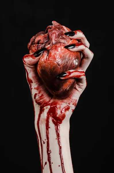 Horror sangrento e tema de Halloween: mãos sangrentas terríveis com unhas pretas segurando um coração humano sangrento em um fundo preto isolado em estúdio — Fotografia de Stock