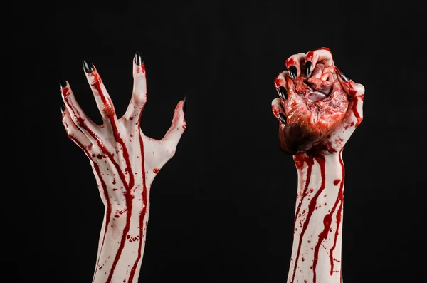 Bloedend, horror en Halloween thema: verschrikkelijk bloedige handen met zwarte nagels houden een bloedige menselijk hart op een zwarte achtergrond geïsoleerd achtergrond in studio — Stockfoto