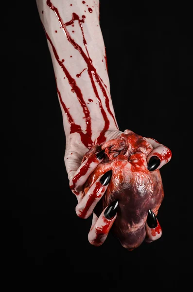Tema sângeroasă de groază și de Halloween: mâini sângeroase teribile cu unghii negre care țin o inimă umană sângeroasă pe un fundal negru izolat în studio — Fotografie, imagine de stoc