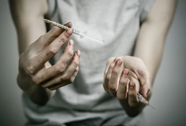 De strijd tegen drugs en drug verslaving onderwerp: mager vuile verslaafde houden van een spuit met een drug en rood hart op een donkere achtergrond — Stockfoto