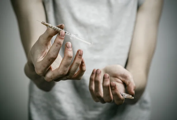 Boj proti drogám a drogové závislosti téma: hubená špinavé narkoman držící injekční stříkačky s drogami a červené srdce na tmavém pozadí — Stock fotografie