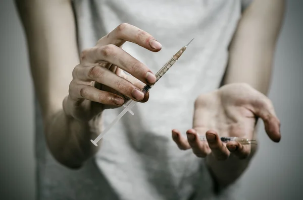 The fight against drugs and drug addiction topic: skinny dirty addict holding a syringe with a drug and red heart on a dark background — Stock Photo, Image