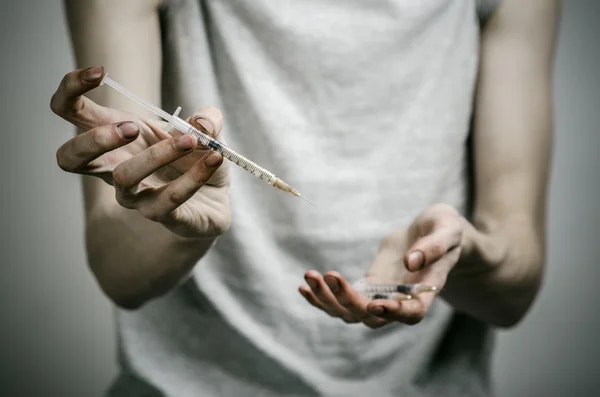 A luta contra as drogas e toxicodependência tópico: viciado sujo magro segurando uma seringa com uma droga e coração vermelho em um fundo escuro — Fotografia de Stock