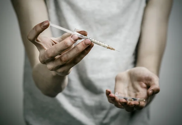 The fight against drugs and drug addiction topic: skinny dirty addict holding a syringe with a drug and red heart on a dark background — Stock Photo, Image