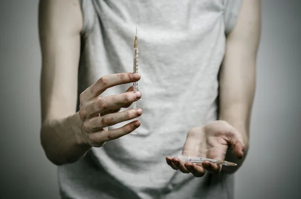 The fight against drugs and drug addiction topic: skinny dirty addict holding a syringe with a drug and red heart on a dark background — Stock Photo, Image