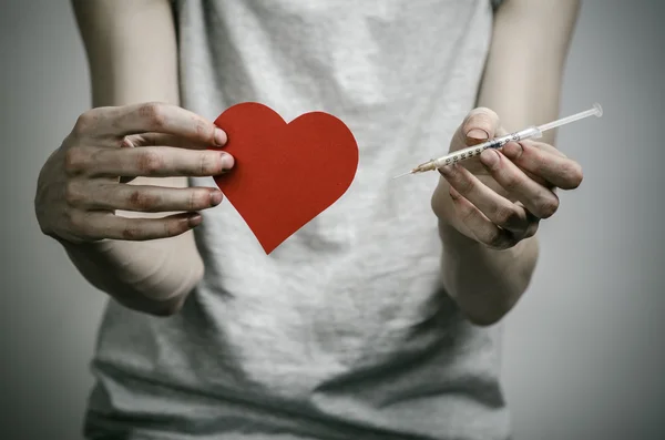 La lucha contra las drogas y la drogadicción tema: adicto sucio flaco sosteniendo una jeringa con una droga y el corazón rojo en un fondo oscuro —  Fotos de Stock