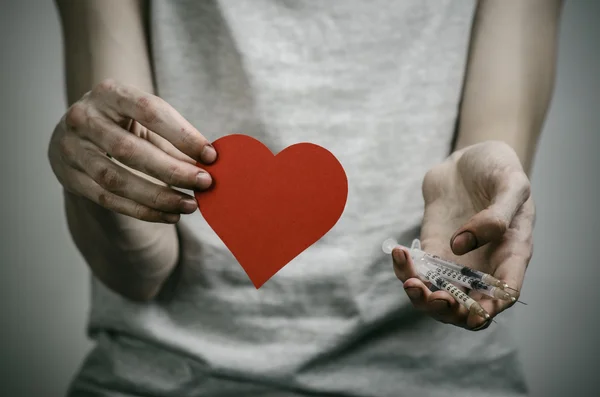 La lucha contra las drogas y la drogadicción tema: adicto sucio flaco sosteniendo una jeringa con una droga y el corazón rojo en un fondo oscuro —  Fotos de Stock