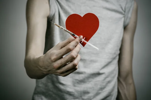 De strijd tegen drugs en drug verslaving onderwerp: mager vuile verslaafde houden van een spuit met een drug en rood hart op een donkere achtergrond — Stockfoto