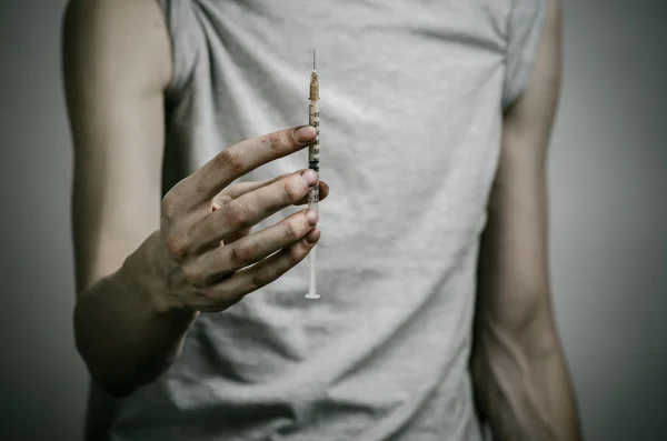 The fight against drugs and drug addiction topic: skinny dirty addict holding a syringe with a drug and red heart on a dark background — Stock Photo, Image