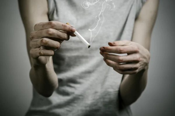 香烟、 成瘾和公共健康主题: 吸烟者认为在他的手和一颗红心在工作室中的黑暗背景上香烟 — 图库照片