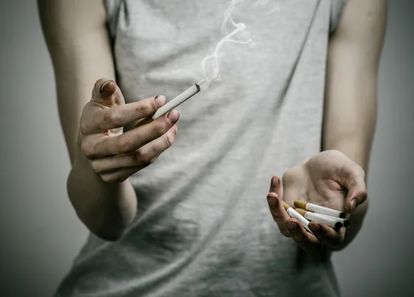 Cigarros, dependência e tópico de saúde pública: fumante segura o cigarro em sua mão e um coração vermelho em um fundo escuro no estúdio — Fotografia de Stock