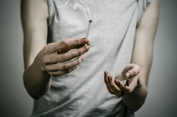 Cigarety, závislosti a veřejného zdraví téma: kuřák má cigaretu v ruce a červené srdce na tmavém pozadí v ateliéru — Stock fotografie