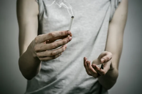 Cigarettes, addiction and public health topic: smoker holds the cigarette in his hand and a red heart on a dark background in the studio — Stock Photo, Image