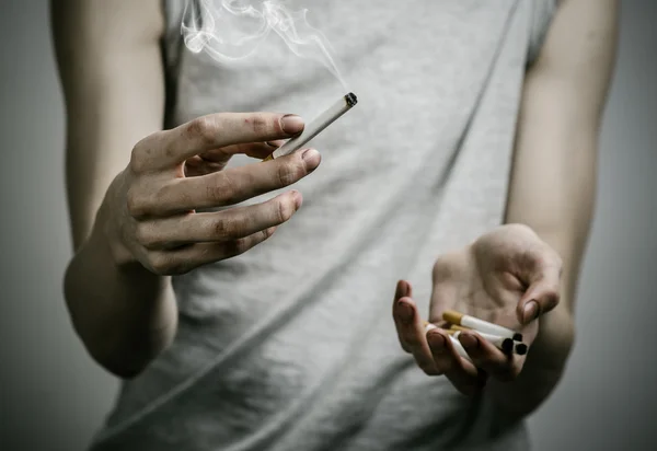 Cigarros, dependência e tópico de saúde pública: fumante segura o cigarro em sua mão e um coração vermelho em um fundo escuro no estúdio — Fotografia de Stock