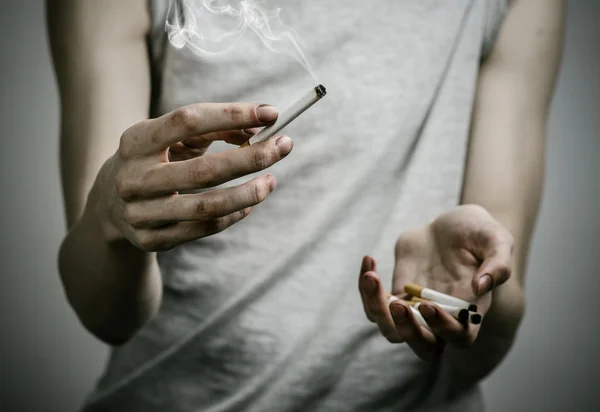 Cigarettes, addiction and public health topic: smoker holds the cigarette in his hand and a red heart on a dark background in the studio — Stock Photo, Image