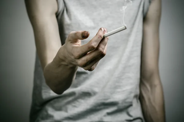 Cigarrillos, adicción y salud pública: el fumador sostiene el cigarrillo en su mano y un corazón rojo sobre un fondo oscuro en el estudio —  Fotos de Stock