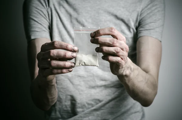 La lucha contra las drogas y la drogadicción tema: adicto sosteniendo paquete de cocaína en una camiseta gris sobre un fondo oscuro en el estudio —  Fotos de Stock