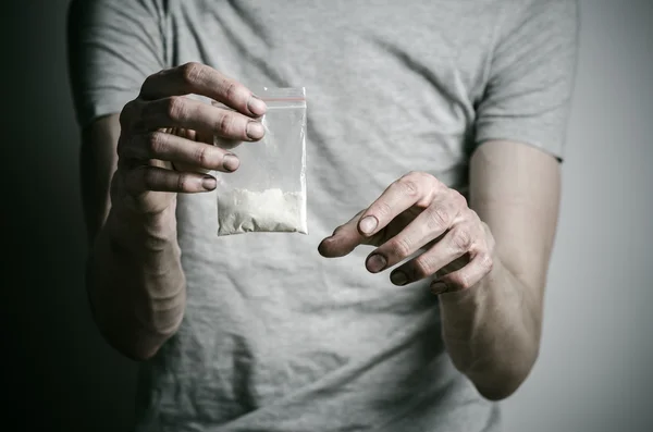 Der Kampf gegen Drogen und Drogenabhängigkeit Thema: Süchtige halten Päckchen mit Kokain in einem grauen T-Shirt vor dunklem Hintergrund im Studio — Stockfoto