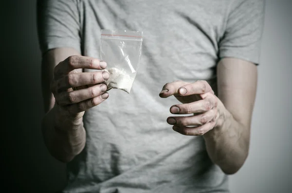 De strijd tegen drugs en drug verslaving onderwerp: verslaafde houden pakket van cocaïne in een grijs T-shirt op een donkere achtergrond in de studio — Stockfoto