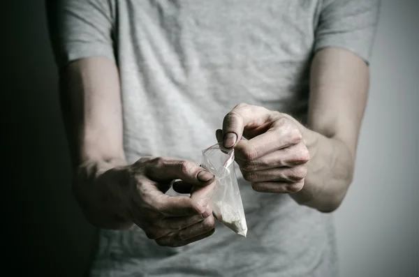 The fight against drugs and drug addiction topic: addict holding package of cocaine in a gray T-shirt on a dark background in the studio — Stock Photo, Image