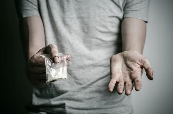 De strijd tegen drugs en drug verslaving onderwerp: verslaafde houden pakket van cocaïne in een grijs T-shirt op een donkere achtergrond in de studio — Stockfoto