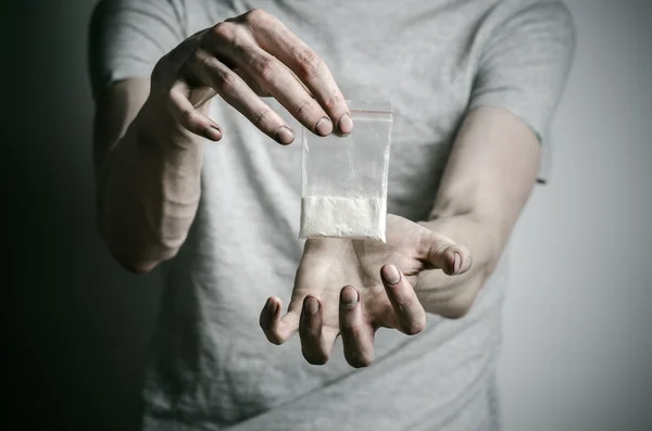 La lucha contra las drogas y la drogadicción tema: adicto sosteniendo paquete de cocaína en una camiseta gris sobre un fondo oscuro en el estudio —  Fotos de Stock