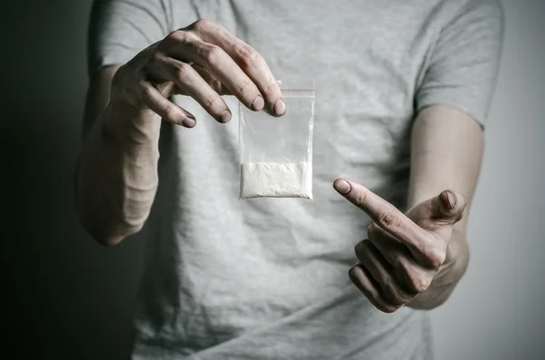 La lucha contra las drogas y la drogadicción tema: adicto sosteniendo paquete de cocaína en una camiseta gris sobre un fondo oscuro en el estudio —  Fotos de Stock