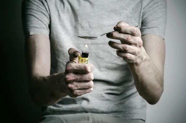 The fight against drugs and drug addiction topic: addict holding spoon lighter and heats the liquid drug in a T-shirt on a dark background — Stock Photo, Image