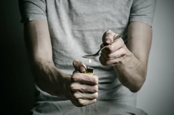 The fight against drugs and drug addiction topic: addict holding spoon lighter and heats the liquid drug in a T-shirt on a dark background — Stock Photo, Image