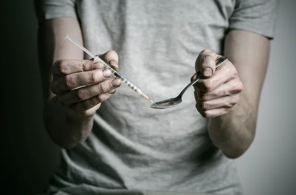 The fight against drugs and drug addiction topic: addict holding spoon lighter and heats the liquid drug in a T-shirt on a dark background — Stock Photo, Image