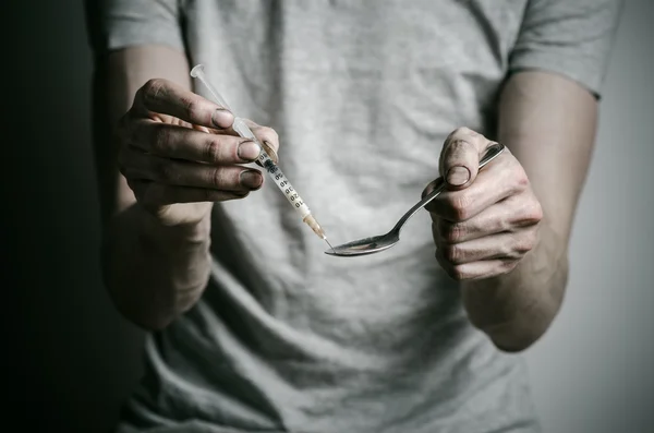 The fight against drugs and drug addiction topic: addict holding spoon lighter and heats the liquid drug in a T-shirt on a dark background — Stock Photo, Image