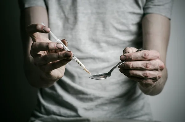 Boj proti drogám a drogové závislosti téma: narkoman držení lžíce světlejší a ohřívá kapalina drog v tričku na tmavém pozadí — Stock fotografie