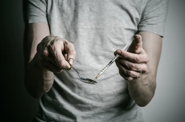 The fight against drugs and drug addiction topic: addict holding spoon lighter and heats the liquid drug in a T-shirt on a dark background — Stock Photo, Image