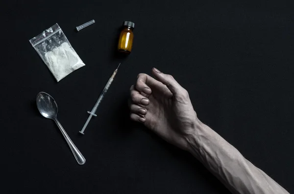 De strijd tegen drugs en drug verslaving onderwerp: hand verslaafde ligt op een donkere tafel en eromheen zijn drugs, een top studio — Stockfoto