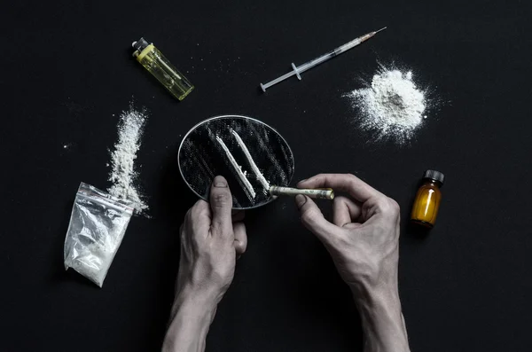 De strijd tegen drugs en drug verslaving onderwerp: hand verslaafde ligt op een donkere tafel en eromheen zijn drugs, een top studio — Stockfoto