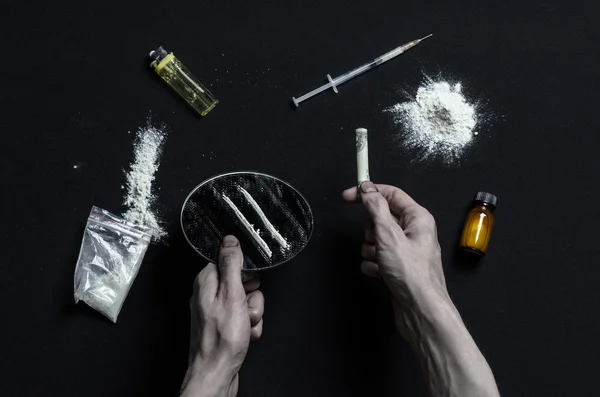 De strijd tegen drugs en drug verslaving onderwerp: hand verslaafde ligt op een donkere tafel en eromheen zijn drugs, een top studio — Stockfoto