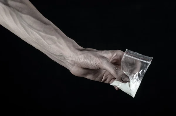 O tema da luta contra as drogas e a toxicodependência: mão suja segurando um saco de cocaína viciada em um fundo preto no estúdio — Fotografia de Stock