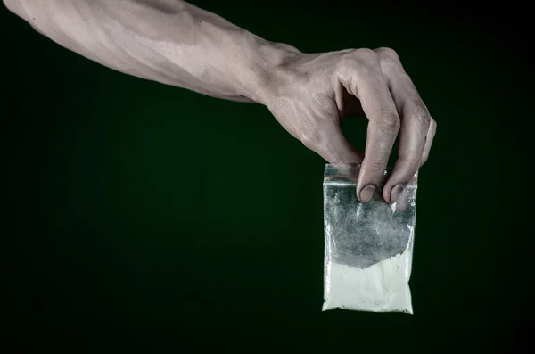 La lucha contra las drogas y la drogadicción tema: mano sucia sosteniendo una bolsa adicta a la cocaína en un fondo verde oscuro en el estudio — Foto de Stock