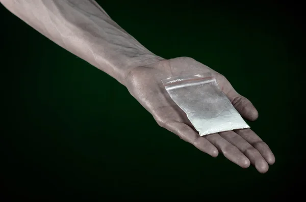 La lucha contra las drogas y la drogadicción tema: mano sucia sosteniendo una bolsa adicta a la cocaína en un fondo verde oscuro en el estudio —  Fotos de Stock