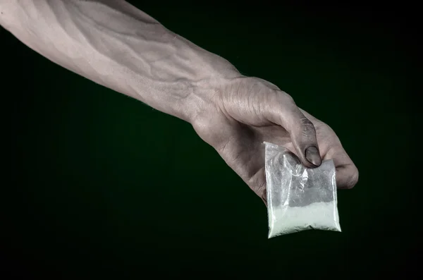 La lucha contra las drogas y la drogadicción tema: mano sucia sosteniendo una bolsa adicta a la cocaína en un fondo verde oscuro en el estudio — Foto de Stock