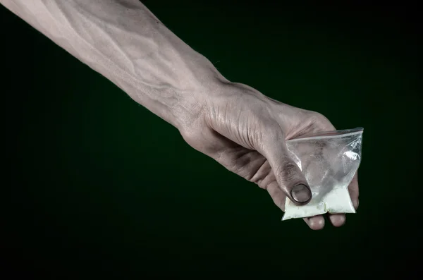 La lucha contra las drogas y la drogadicción tema: mano sucia sosteniendo una bolsa adicta a la cocaína en un fondo verde oscuro en el estudio — Foto de Stock