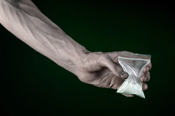 La lucha contra las drogas y la drogadicción tema: mano sucia sosteniendo una bolsa adicta a la cocaína en un fondo verde oscuro en el estudio — Foto de Stock