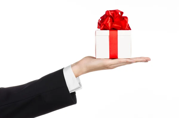 Il tema delle celebrazioni e dei regali: un uomo in abito nero con in mano un regalo esclusivo avvolto in scatola bianca con nastro rosso e fiocco, il regalo più bello isolato su sfondo bianco in studio — Foto Stock