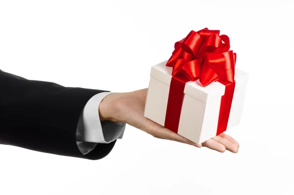 El tema de las celebraciones y regalos: un hombre en un traje negro con un regalo exclusivo envuelto en una caja blanca con cinta roja y lazo, el regalo más hermoso aislado sobre fondo blanco en el estudio — Foto de Stock