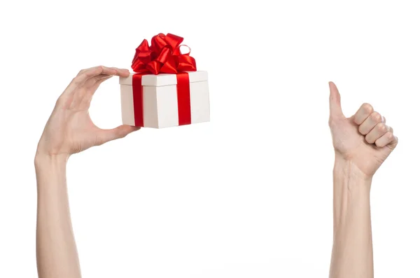 Le thème des célébrations et des cadeaux : main tenant un cadeau enveloppé dans une boîte blanche avec ruban rouge et arc, le plus beau cadeau isolé sur fond blanc en studio — Photo