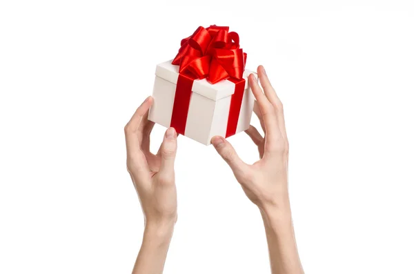 Le thème des célébrations et des cadeaux : main tenant un cadeau enveloppé dans une boîte blanche avec ruban rouge et arc, le plus beau cadeau isolé sur fond blanc en studio — Photo