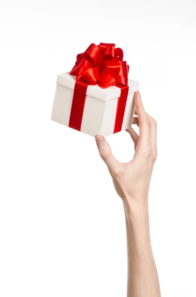 Het thema van vieringen en giften: hand met een geschenk verpakt in witte doos met rood lint en boog, het mooiste geschenk geïsoleerd op een witte achtergrond in studio — Stockfoto