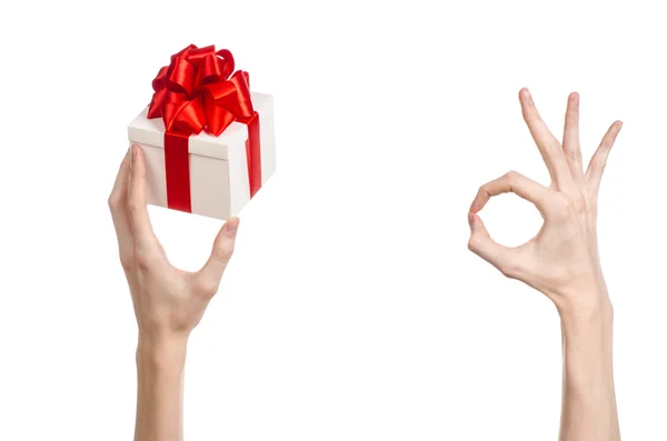 El tema de las celebraciones y regalos: la mano sosteniendo un regalo envuelto en caja blanca con cinta roja y lazo, el regalo más hermoso aislado sobre fondo blanco en el estudio — Foto de Stock